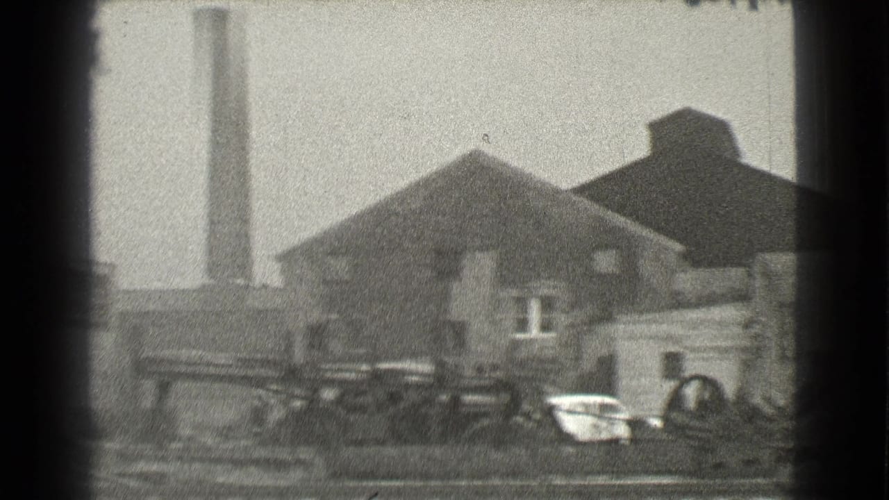 1939 Cleveland home-movie frame showing a brick industrial building, tall smokestack, and cluttered yard foreground.
