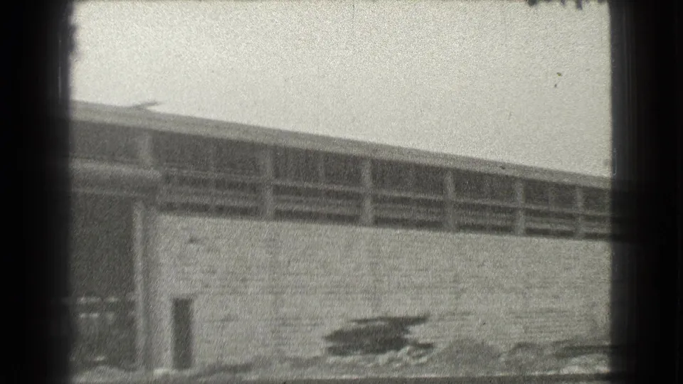 Black-and-white 8mm view of a Cleveland industrial building with upper window rows, brick wall, and leafless trees.