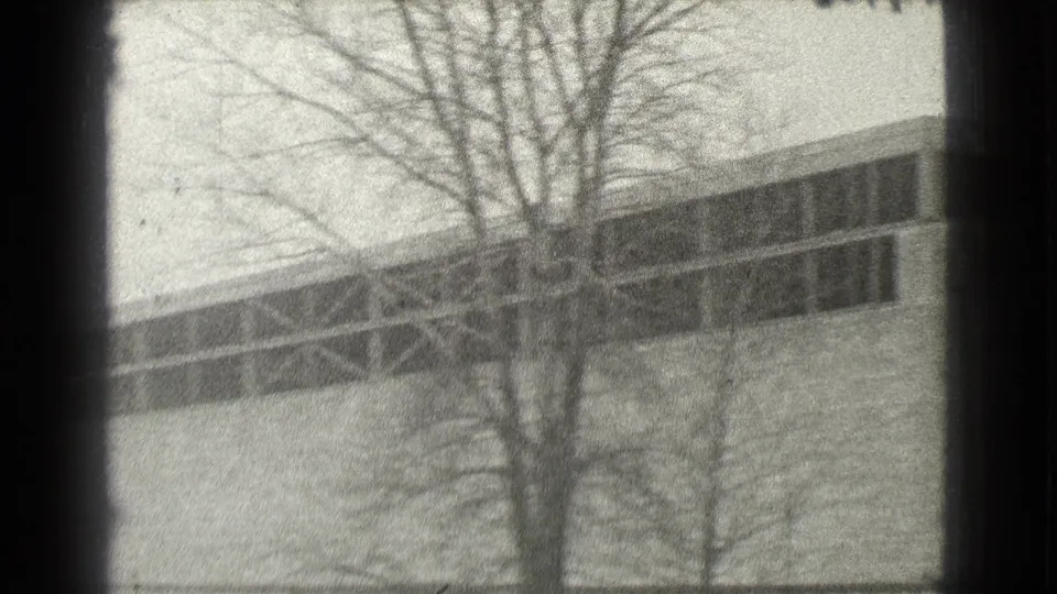 1939 Cleveland home-movie frame showing a long utilitarian building partly obscured by bare trees.