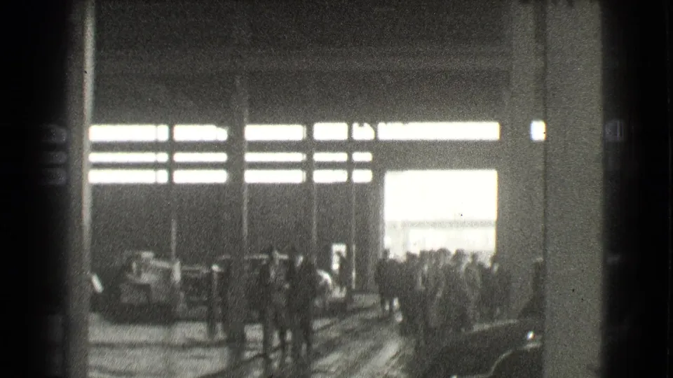 1939 Cleveland factory interior with silhouetted workers gathering near columns and bright horizontal window light.