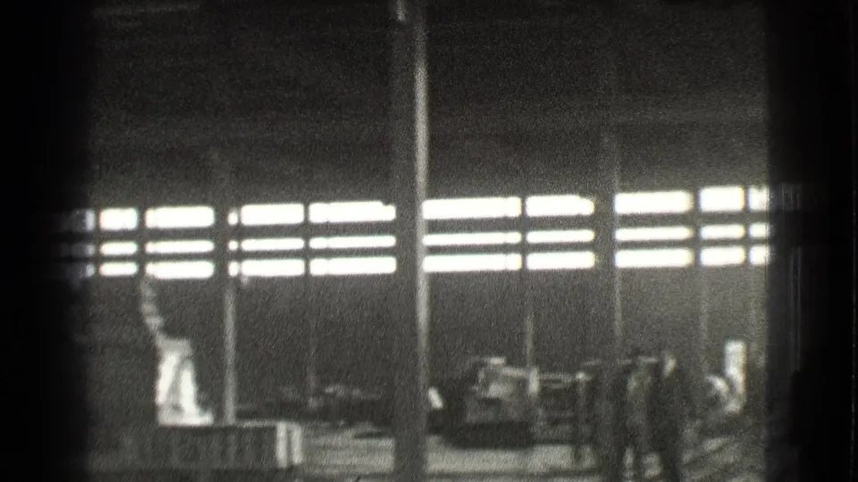 Black-and-white 1939 Cleveland factory view with workers clustered near equipment under bright window bands.