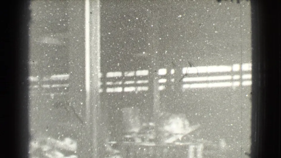 Soft black-and-white 8mm view inside a 1939 Cleveland factory, with columns, window light and indistinct work areas.