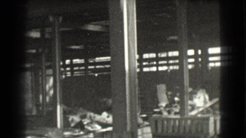 1939 Cleveland home-movie frame showing a dark factory-like room with vertical columns, high window light, and floor debris.