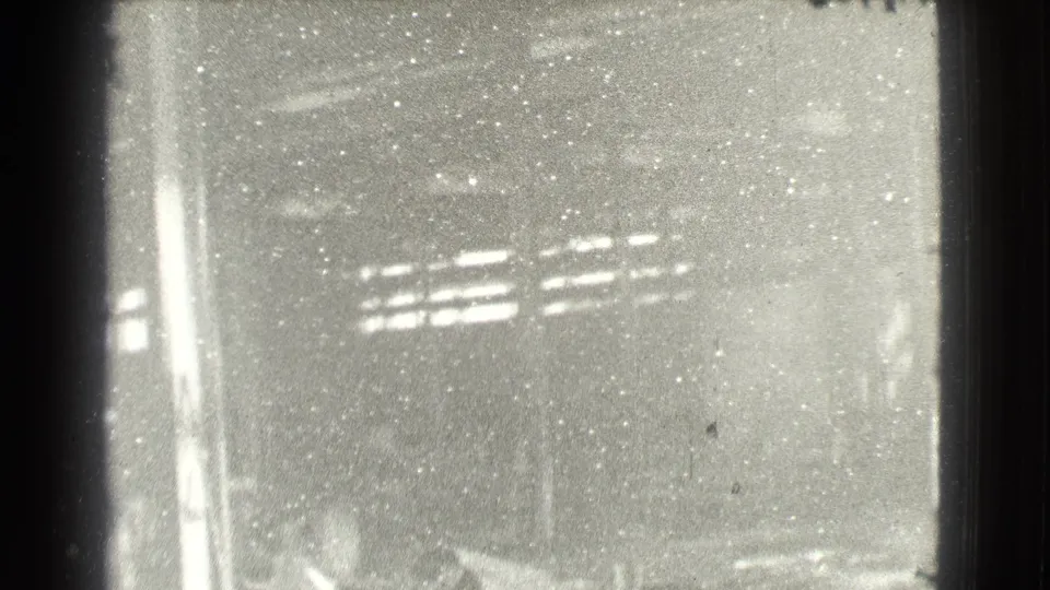 The 8mm frame blooms brighter during the pan, with columns, high slatted windows, and heavy film speckling visible.