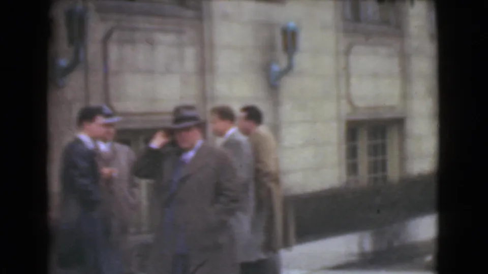 Adult men in 1930s-style suits, coats, and hats appear in conversation outside a stone building in Cleveland, Ohio.