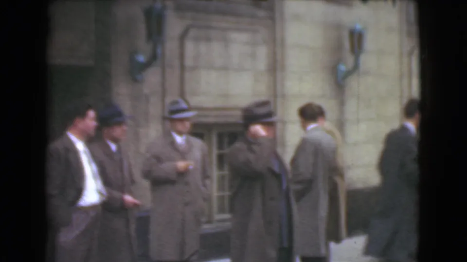 Cleveland 1939 street footage shows suited adult men in hats standing and moving near a stone building with basement-level windows.