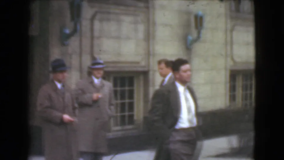 Adult men in suits and brimmed hats appear outside a Cleveland stone building, with one man passing close to the camera.