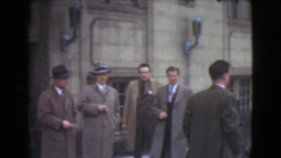 In supported 1939 Cleveland home-movie footage, several men in suits and fedoras gather outside a masonry building on a city street.