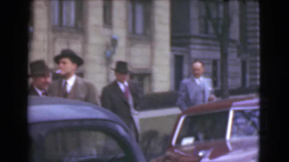 A small group of men in fedoras and suits stands near parked cars outside a Cleveland building in this 1939 home-movie frame.
