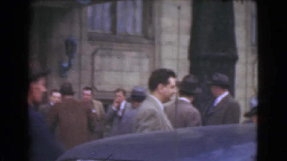 A suited man passes through the foreground as other men stand near a stone building entrance in Cleveland, 1939.