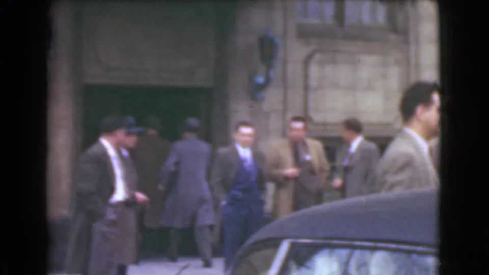 Men in suits and hats appear to enter or gather at a Cleveland building doorway, seen behind a dark automobile foreground.
