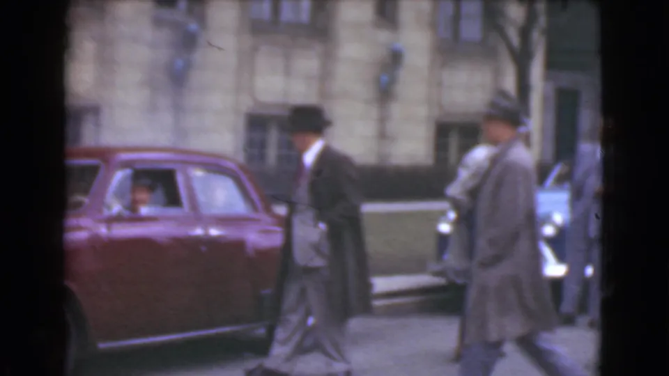 Two hatted men, one in a dark coat and one in a lighter coat, walk near the maroon sedan in the Cleveland street footage.