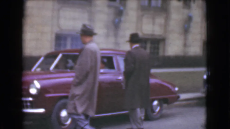 At the end of the 1939 Cleveland clip, two men in coats and hats stand near the front and side of a maroon sedan.