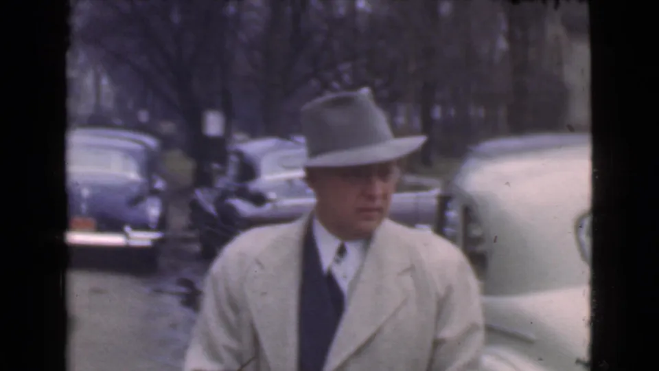 The man appears closer to the camera, looking down as parked automobiles and leafless trees line the Cleveland street.
