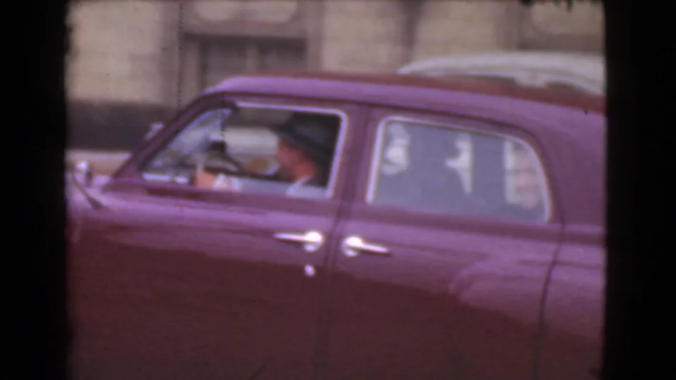 A red late-1930s sedan moves through the Cleveland street scene, with the driver visible through the side window.