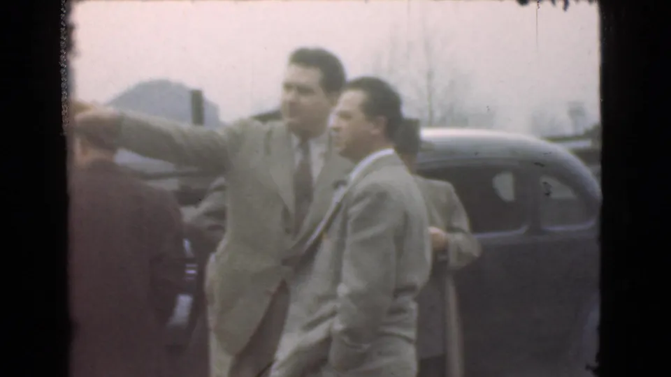 A suited man gestures toward the distance beside another man and a dark car in 1939 Cleveland home-movie footage.
