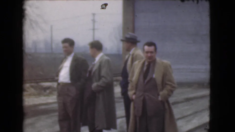 Five men in coats and suits stand outdoors in Cleveland, with one man looking toward the camera in soft 8mm footage.