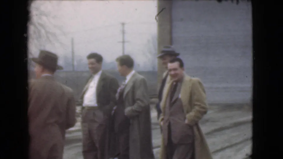 Adult men in suits, overcoats, and hats appear to converse outdoors in Cleveland, Ohio, with utility poles behind them.