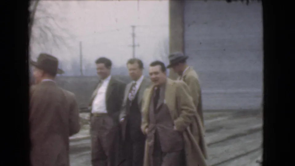 In this 1939 Cleveland home-movie frame, several adult men in suits and coats stand outdoors, with one face turned toward the camera.