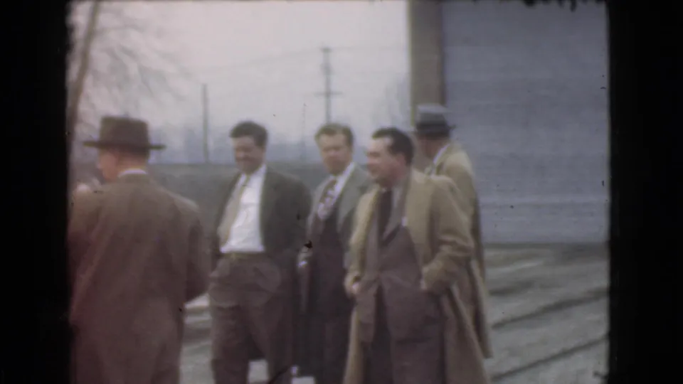 Adult men in 1939 Cleveland clothing stand outside near a plain building wall, with hats, overcoats, and utility poles visible.