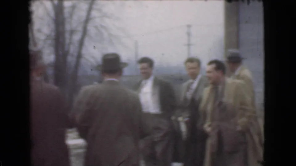 In 1939 Cleveland home-movie footage, suited men in hats gather outdoors near bare trees and utility poles.