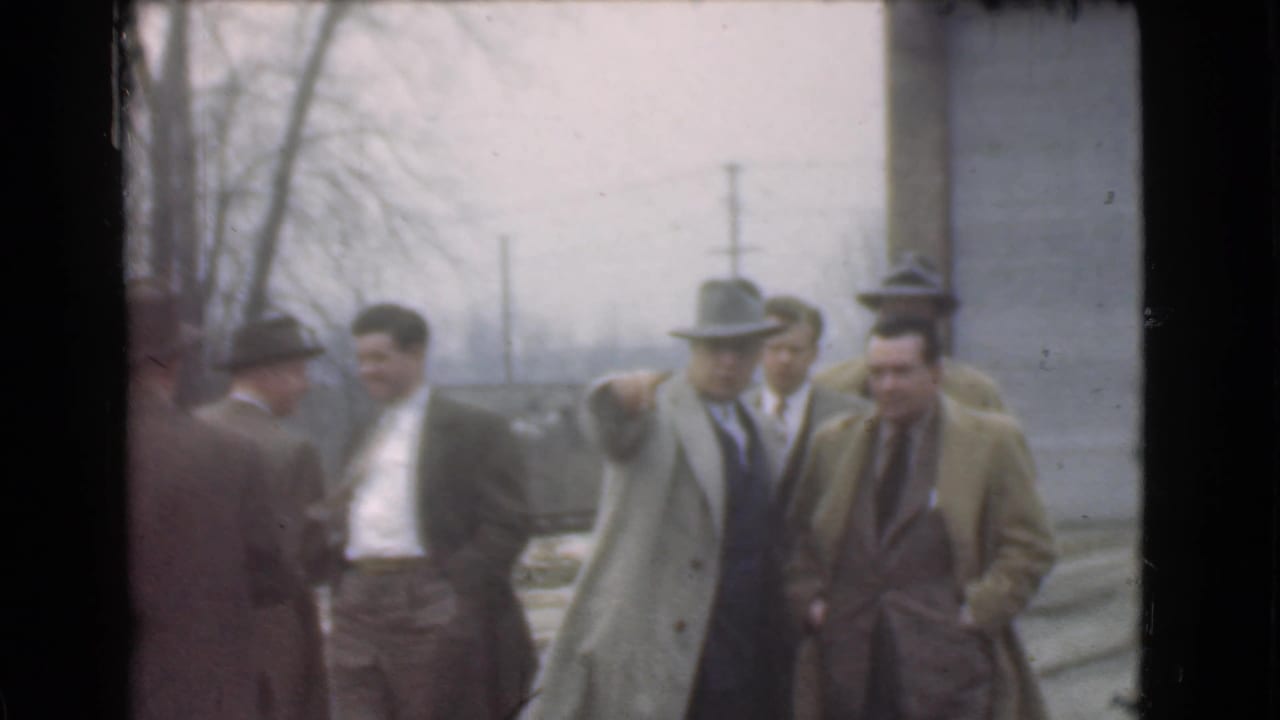 Several men in coats and hats talk while walking outdoors.