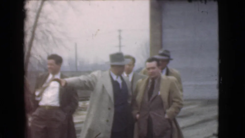 One man in a light overcoat gestures toward the left while other suited men stand nearby in the 1939 Cleveland scene.