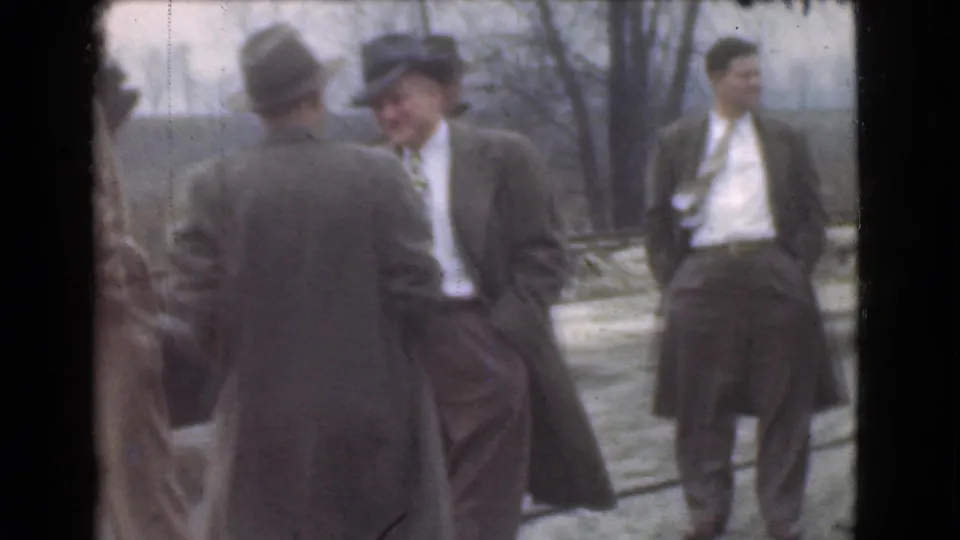 In 1939 Cleveland home-movie footage, several adult men in suits, fedoras, and overcoats gather outdoors near a roadside.