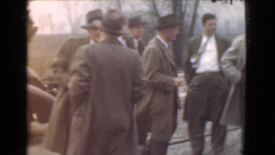 Several adult men in 1930s-style suits, fedoras, and overcoats stand outdoors in Cleveland, appearing to continue a casual conversation.