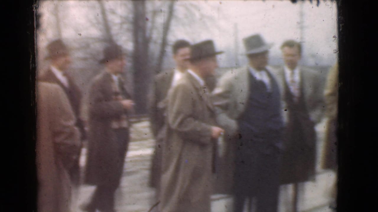 In supported 1939 Cleveland home-movie footage, adult men in fedoras and overcoats gather outdoors and converse near bare trees.