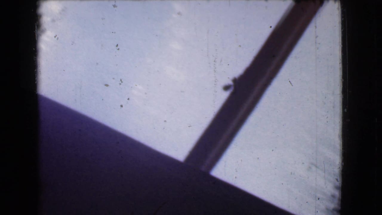 Dark diagonal window or structural frame crosses a pale sky or light surface.