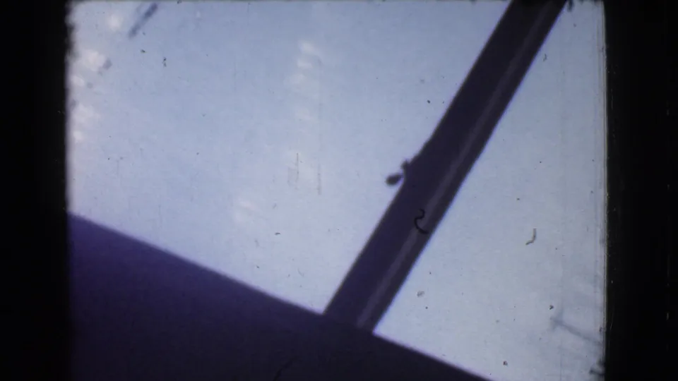 The camera holds on an angled dark frame beside a pale light area, with visible 8mm grain, dust, and scratches.