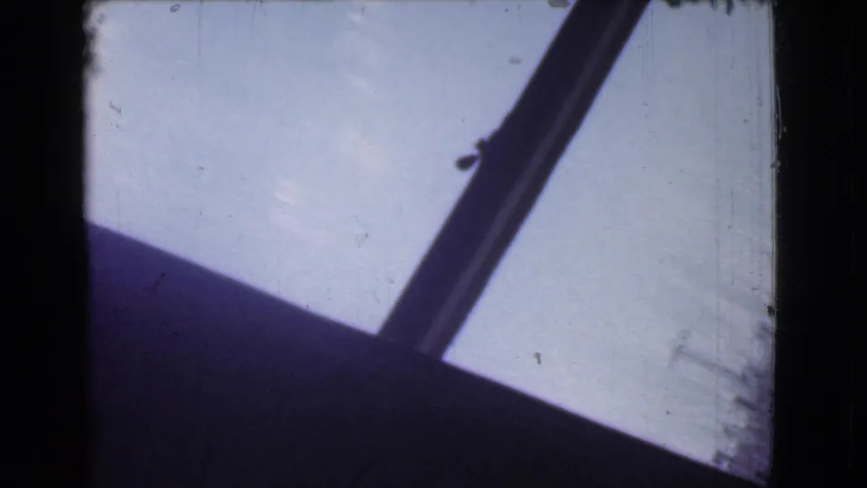 A diagonal dark structural line crosses a pale sky or glass surface, with the lower part of the frame falling into shadow.