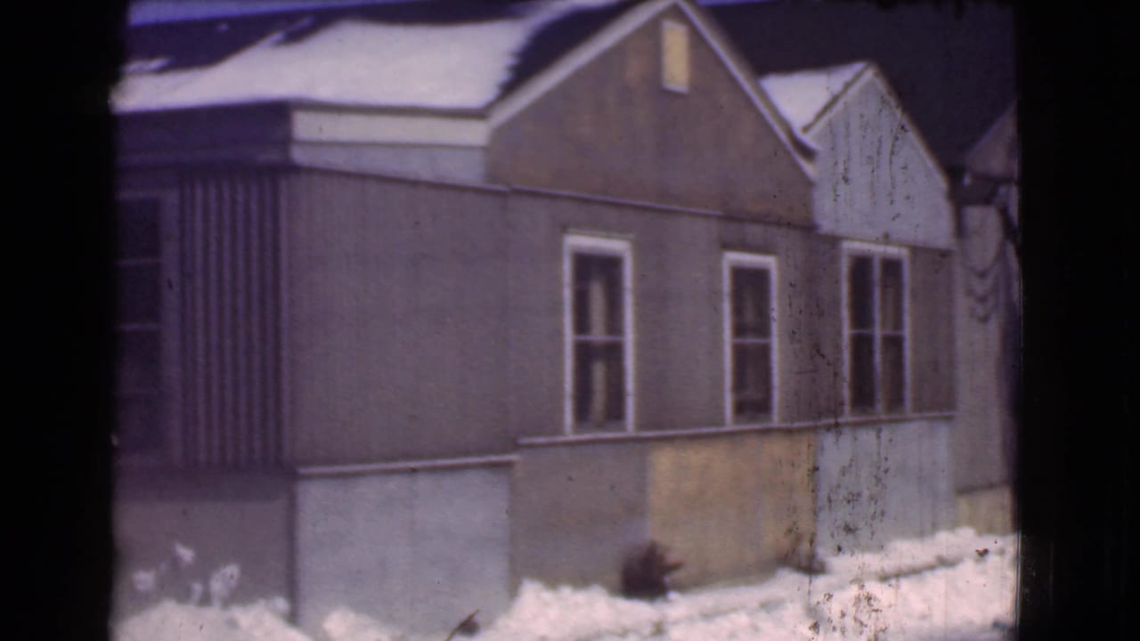 Closer view of the brown house wall, windows, siding, and snow along the ground.