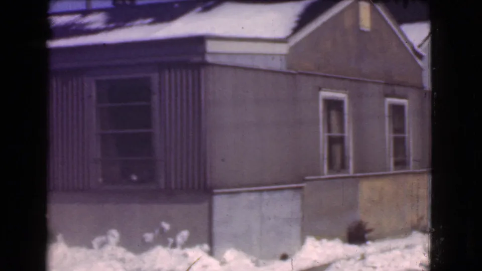 1939 Cleveland 8mm frame showing the side portion of a brown house, corrugated siding, white-trimmed windows, and snowbanks.