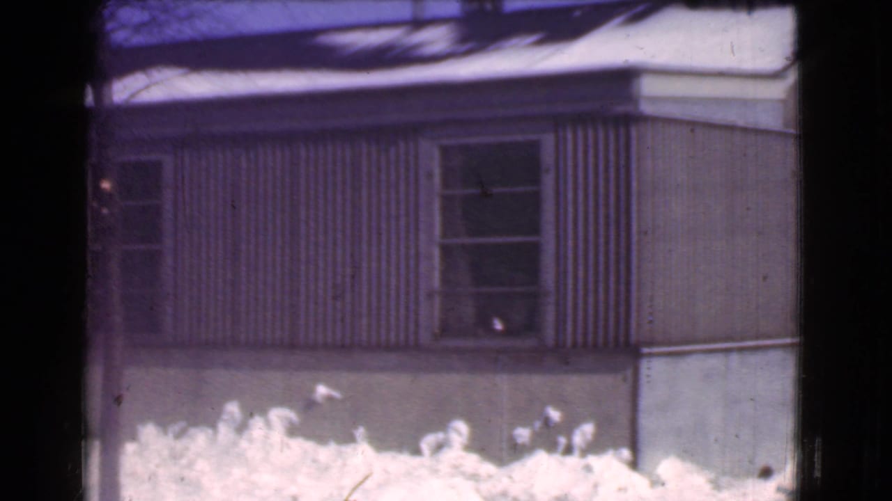 Snowbank in front of a corrugated building wall with windows and a dark foreground pole.