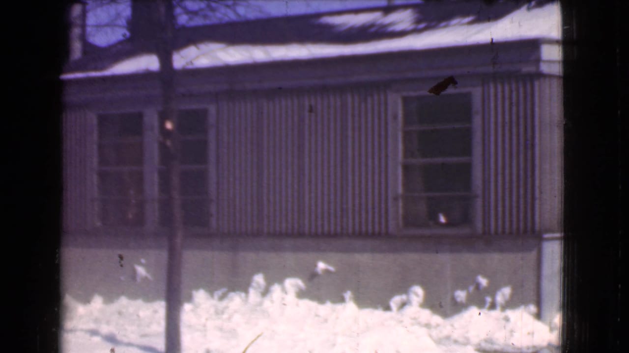 1939 Cleveland winter frame with a snow-covered foreground, corrugated siding, two windows, and dark vertical obstructions near the camera.