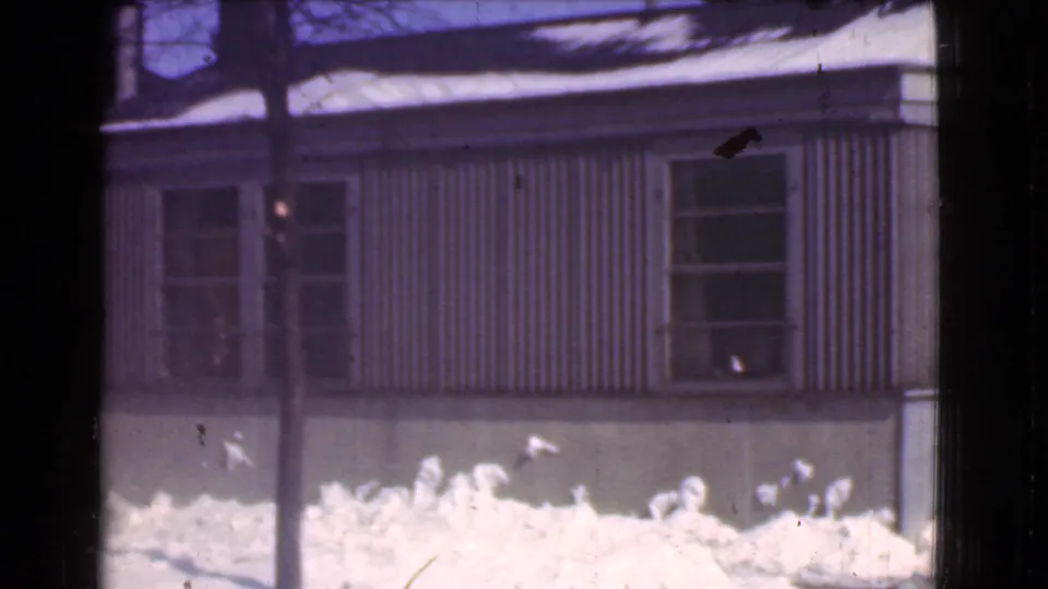 1939 Cleveland winter frame with a snow-covered foreground, corrugated siding, two windows, and dark vertical obstructions near the camera.