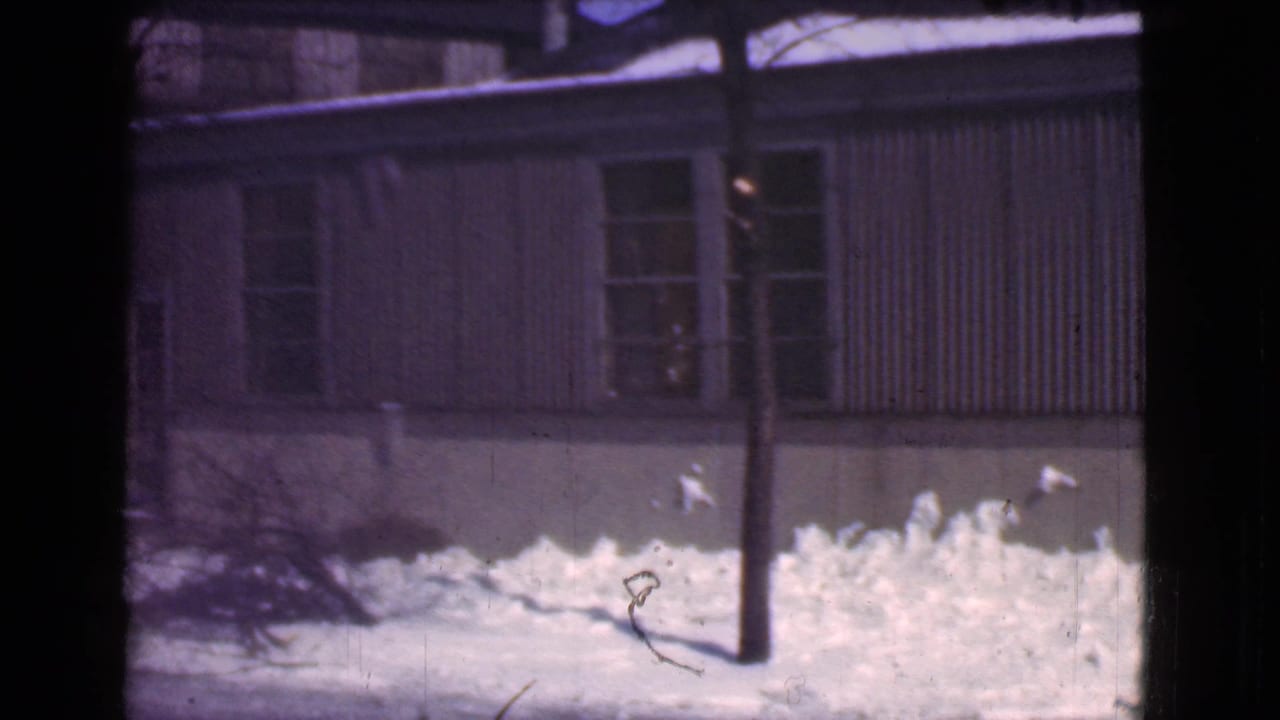 1939 Cleveland home-movie frame showing snowbanks, a modest building, a utility pole, and dark film gate edges.