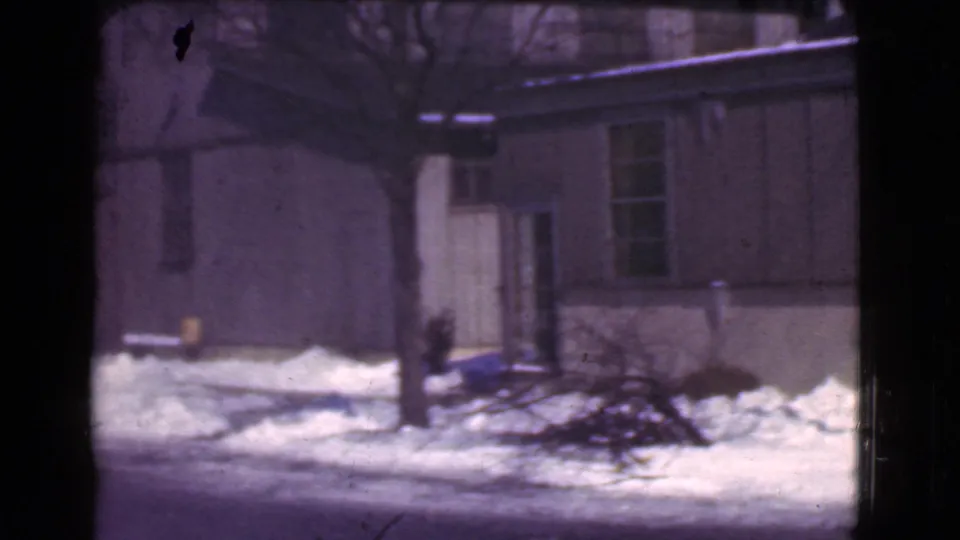 1939 Cleveland frame showing a snow-covered street edge, building wall, utility pole, bare trees, and stacked brush.