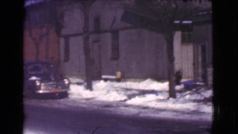 1939 Cleveland winter frame with a parked rounded automobile, snowbanks, bare trees, and a modest residential building.