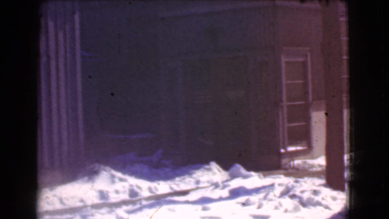 Snow piled in front of a dark storefront with a glass-paneled door at right.