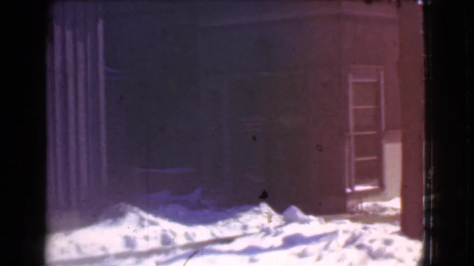 Final 8mm frame of a snowy Cleveland storefront exterior, showing deep drifts and a glass-paneled door.