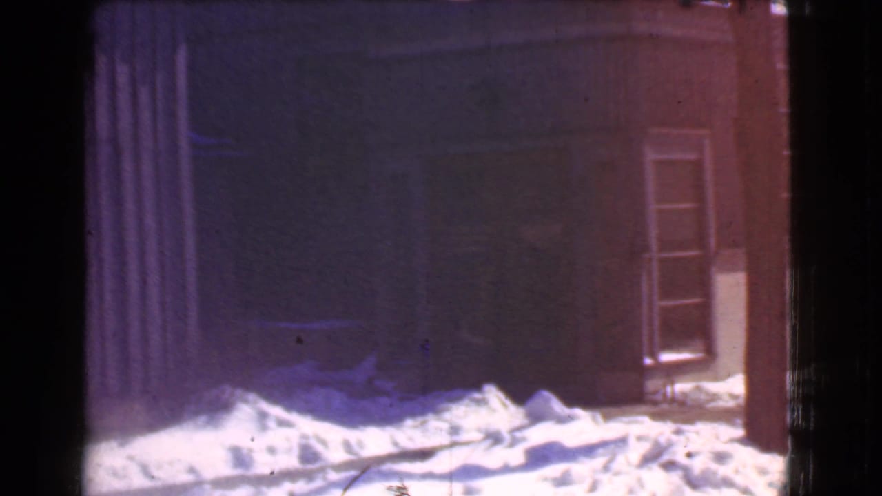 Snow piled before a dark commercial building with windows and a narrow vertical facade.