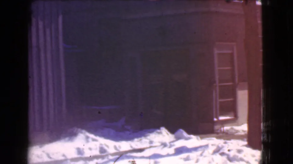 1939 Cleveland 8mm frame showing snowbanks outside a dark storefront or commercial building with windows and soft purple-red film color.