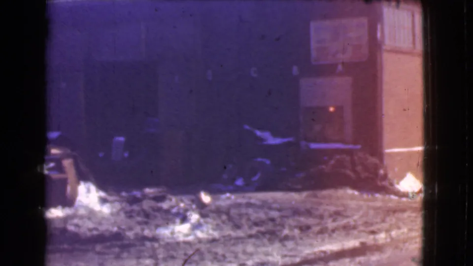 1939 Cleveland 8mm frame showing a snow-covered street edge, commercial windows, a vertical facade, and dark clutter near the building base.