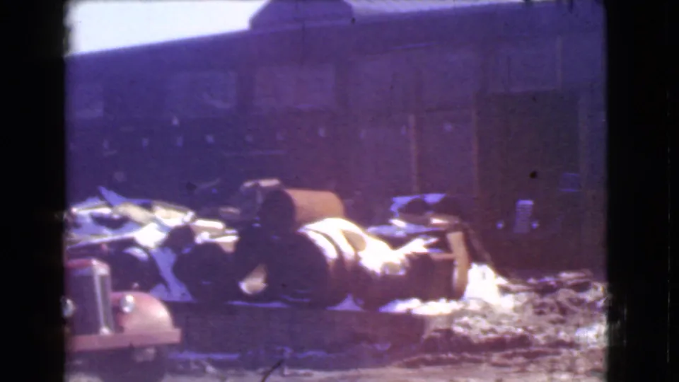 1939 Cleveland frame showing the same warehouse yard from a static angle, with drums, debris, and wintery ground texture.
