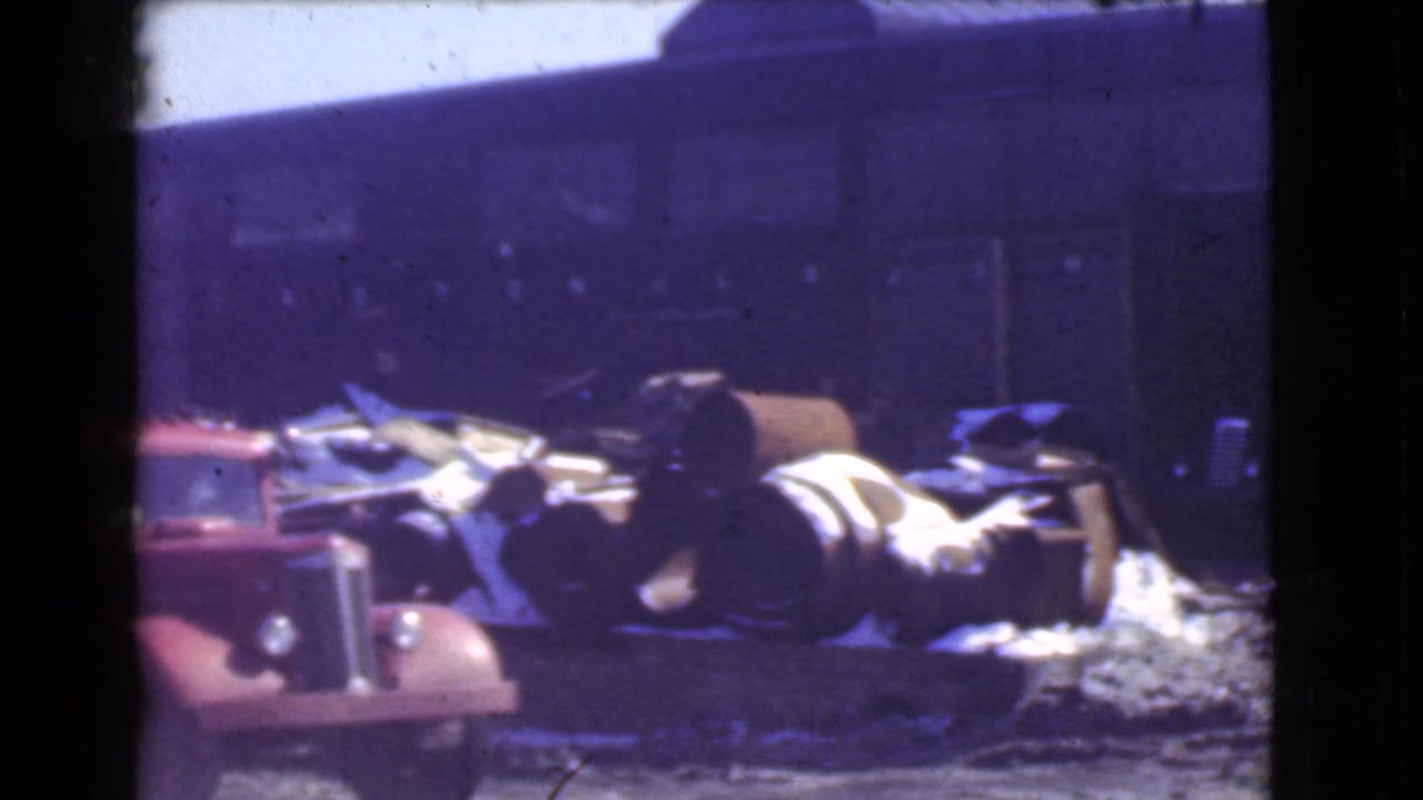 A red late-1930s truck sits near metal barrels and scattered debris outside a dark factory building in Cleveland, Ohio.