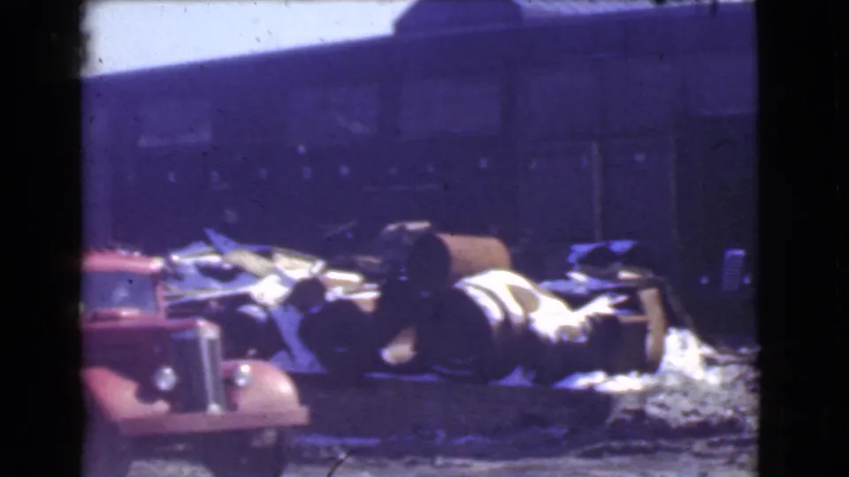 A red late-1930s truck sits near metal barrels and scattered debris outside a dark factory building in Cleveland, Ohio.