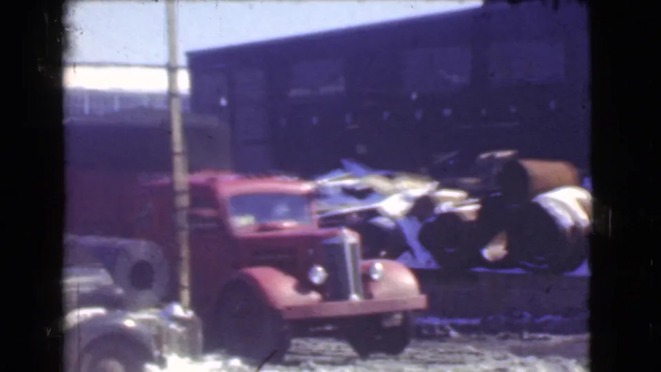 A red truck remains parked near a utility pole, with barrels, debris, snow, and a dark industrial building filling the background.